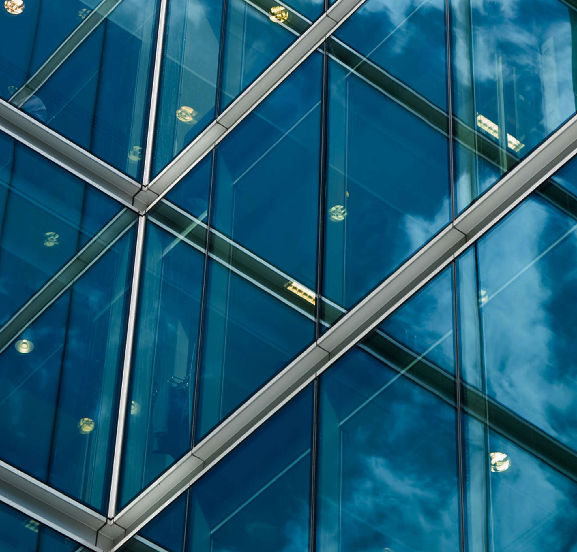 Reflective windows on a building reflecting lights, a blue sky with clouds, and other windows.