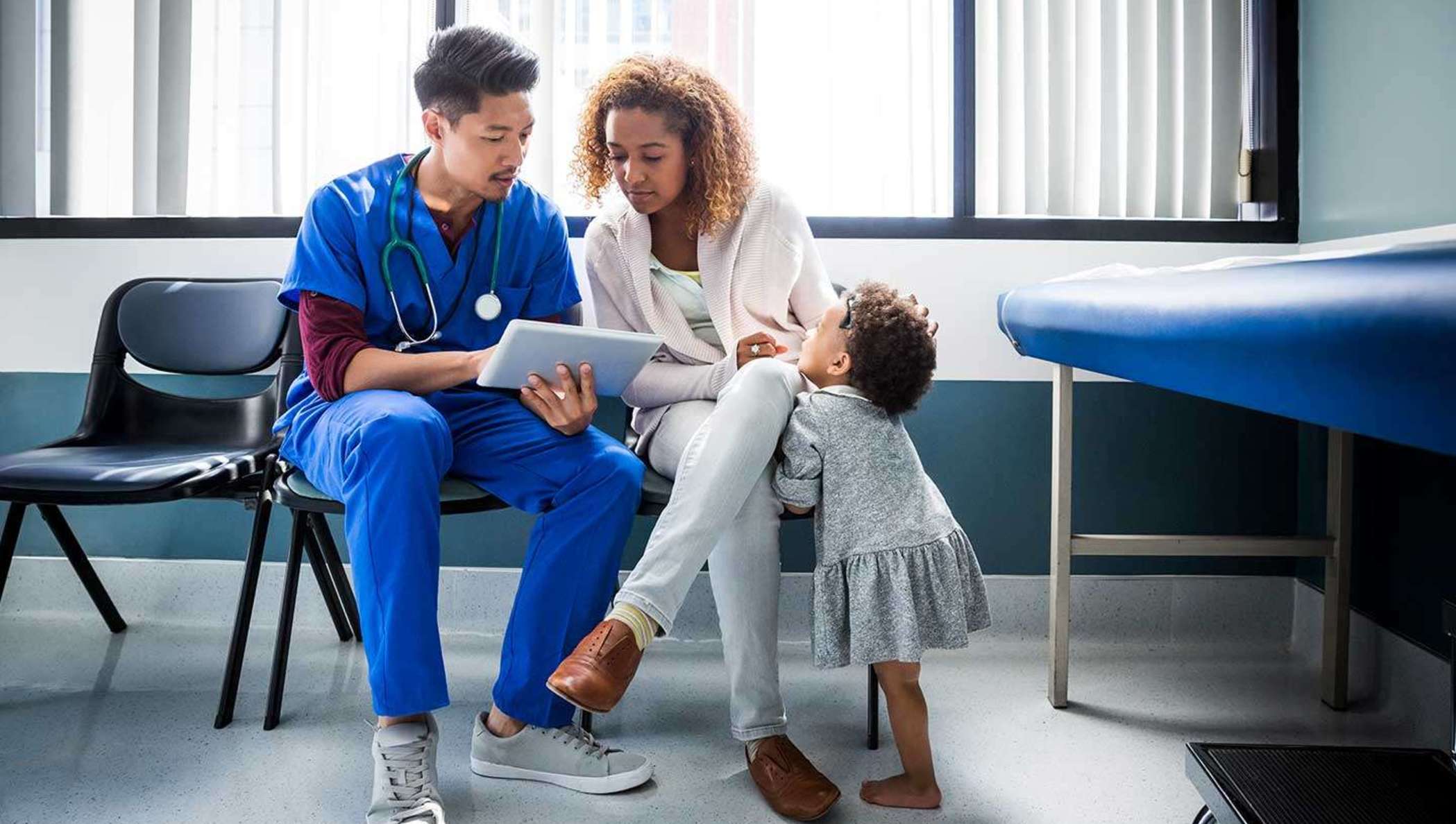 Um médico mostrando informações em um iPad para uma mãe e um filho em um quarto de hospital.