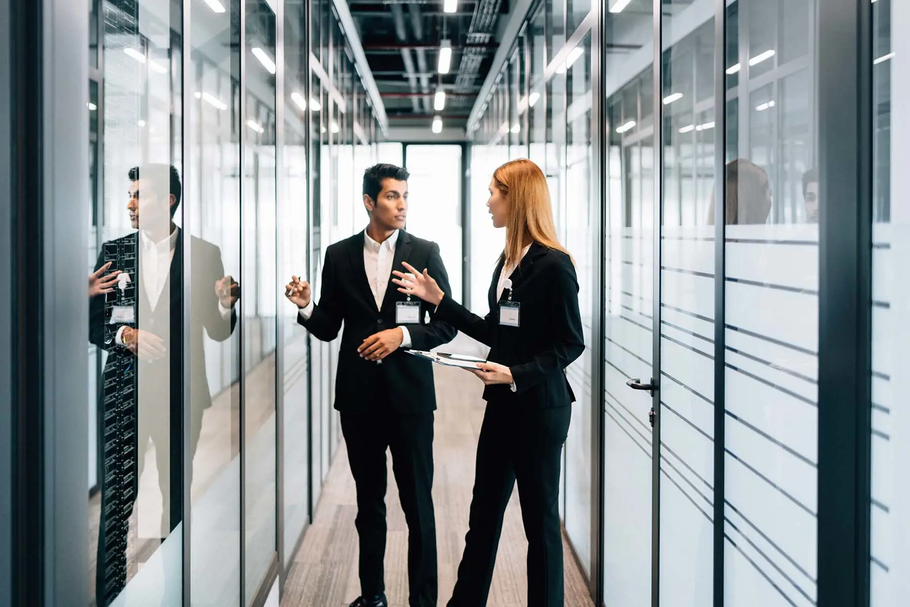 Dois colegas de trabalho conversando no corredor de um escritório corporativo