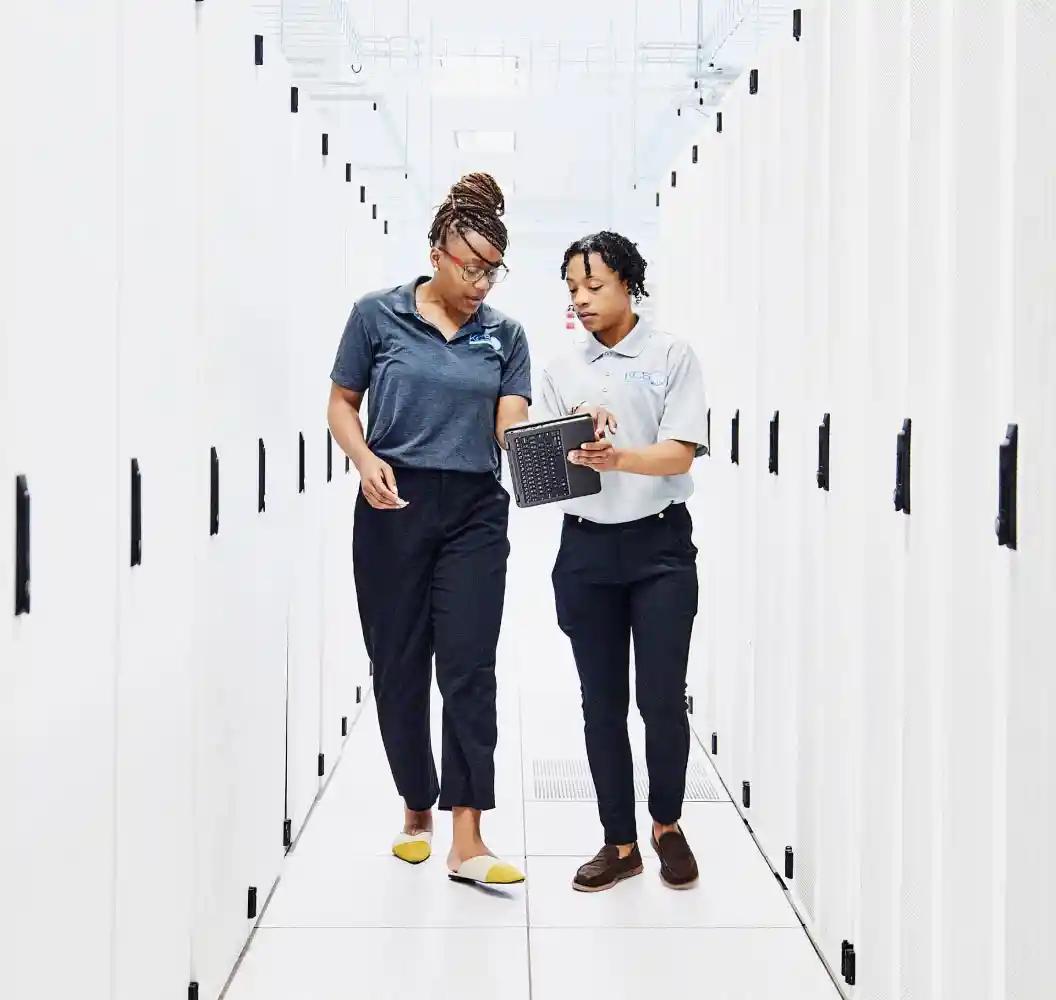 Female IT professionals looking at data on digital tablet in a data center.
