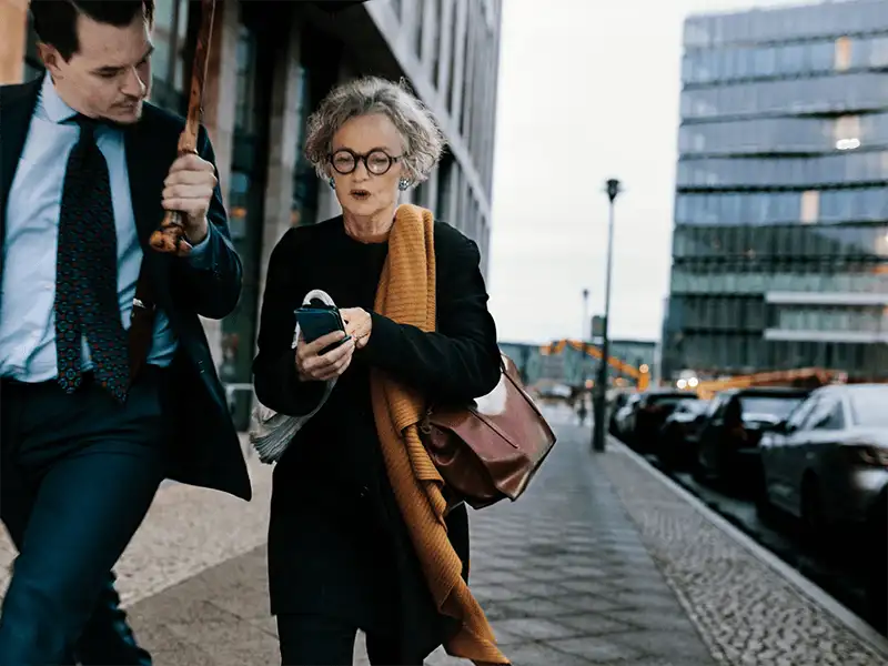 街の通りを歩いている女性と男性が、女性の携帯電話を眺める