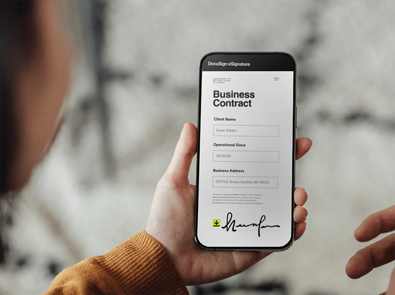 Person holding phone showing DocuSign logo while working on a laptop