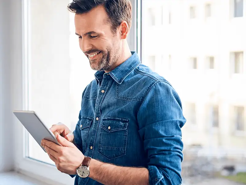 Hombre que sonría y sostiene una Tablet e interactúa con la pantalla