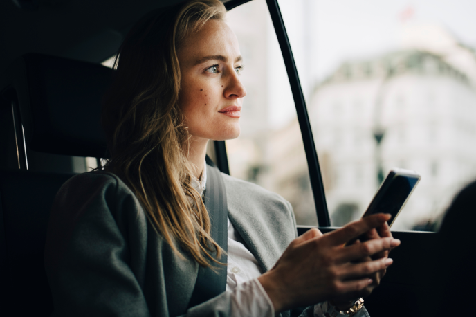 Uma mulher olhando através da janela do carro com um celular nas mãos.